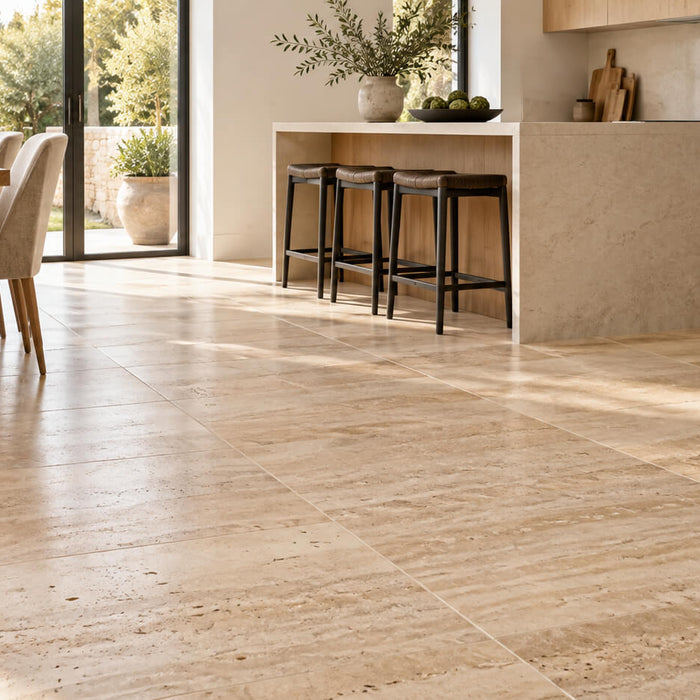 Sunlit kitchen with beige travertine floor tiles, oak cabinetry and upholstered dining chairs.