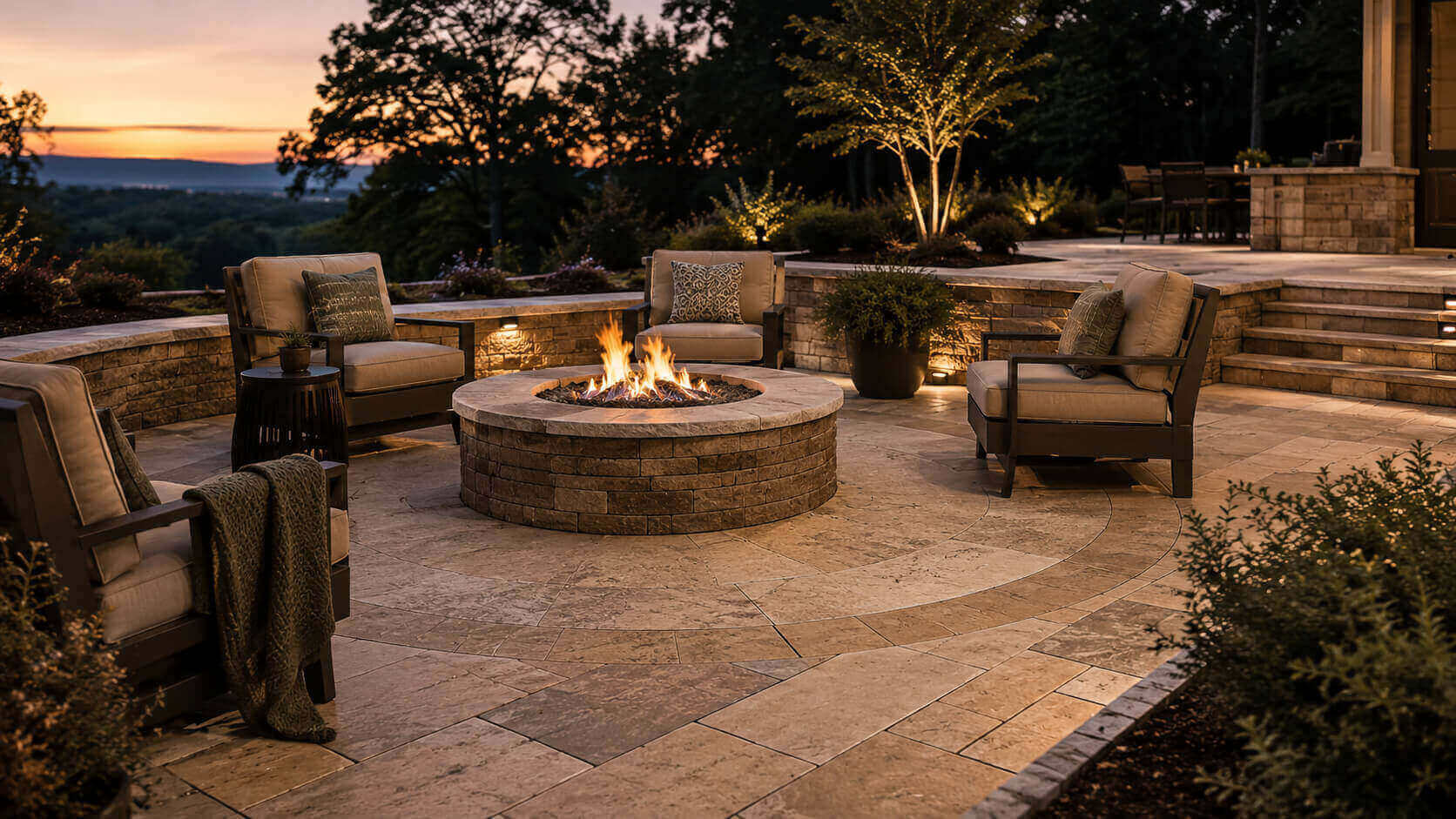 Luxury outdoor fire pit patio with natural stone pavers, seating, and landscape lighting at sunset