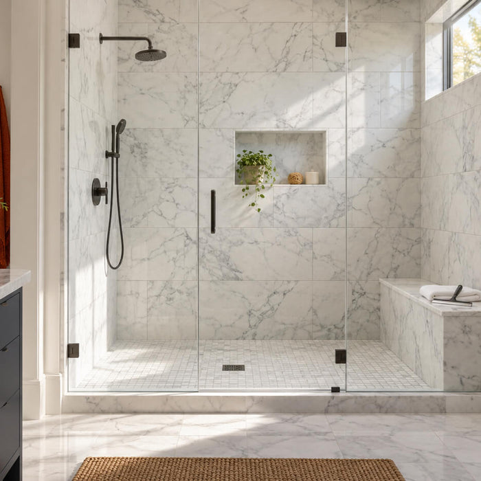 White marble shower with gray veining, black fixtures, and a microfiber cloth and squeegee on a marble bench.