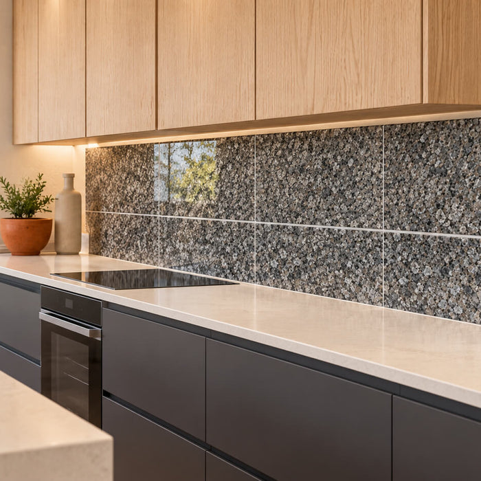 Close-up of gray granite backsplash tiles with a polished exposed edge beside a cream wall and wood cabinetry.