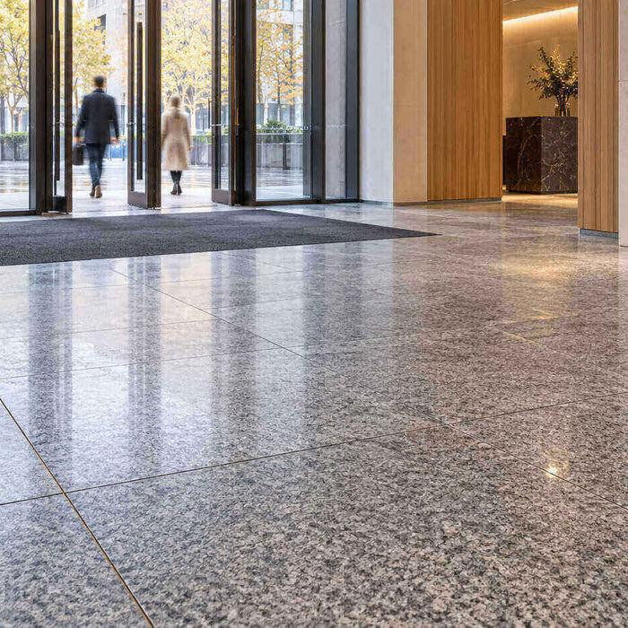 Gray granite floor tiles in a modern entrance lobby with a recessed mat, glass doors, and an orange bench.