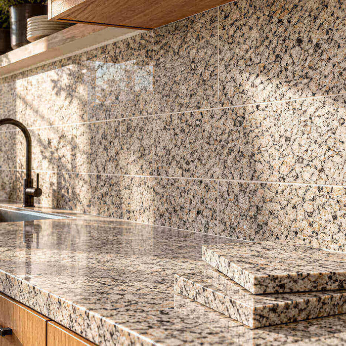 Sunlit kitchen with a speckled granite tile backsplash, oak cabinets, and stacked granite samples on the countertop.