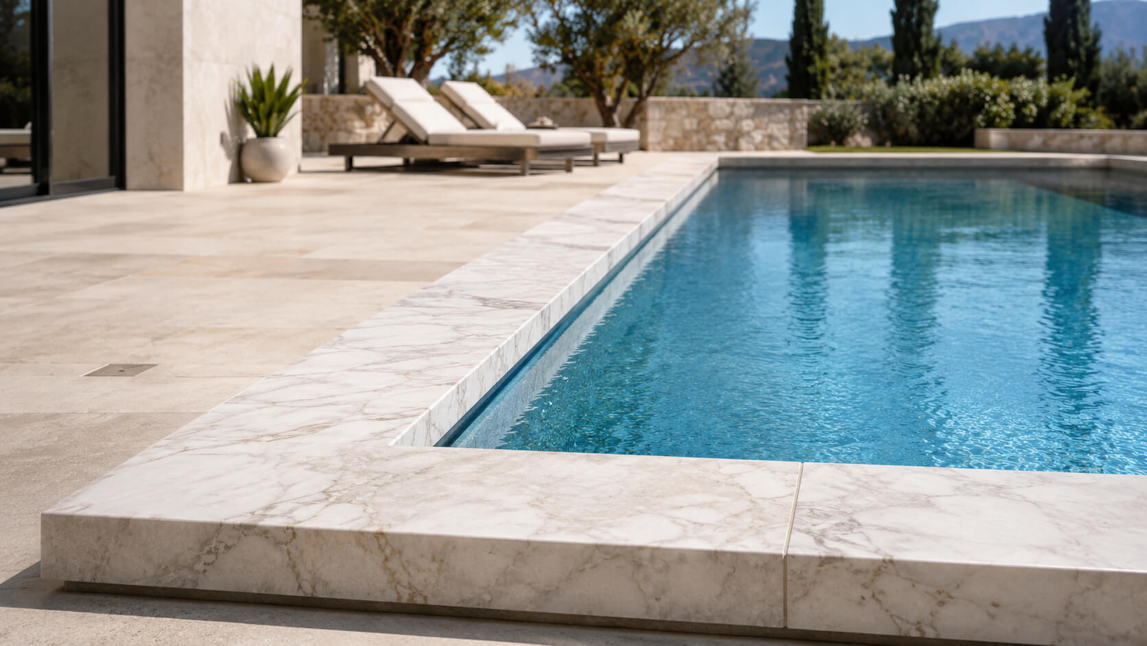 Light marble coping surrounding a luxury outdoor swimming pool with natural stone decking