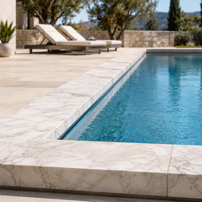 Light marble coping surrounding a luxury outdoor swimming pool with natural stone decking