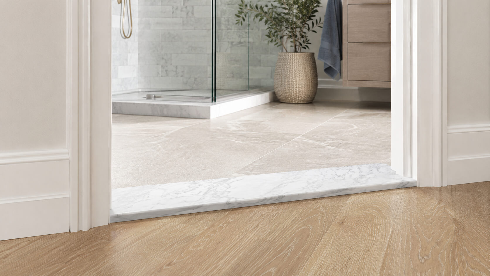 White marble threshold creating a clean transition between bathroom tile and light wood flooring