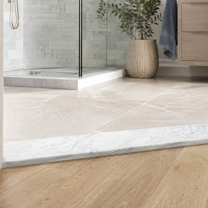 White marble threshold creating a clean transition between bathroom tile and light wood flooring