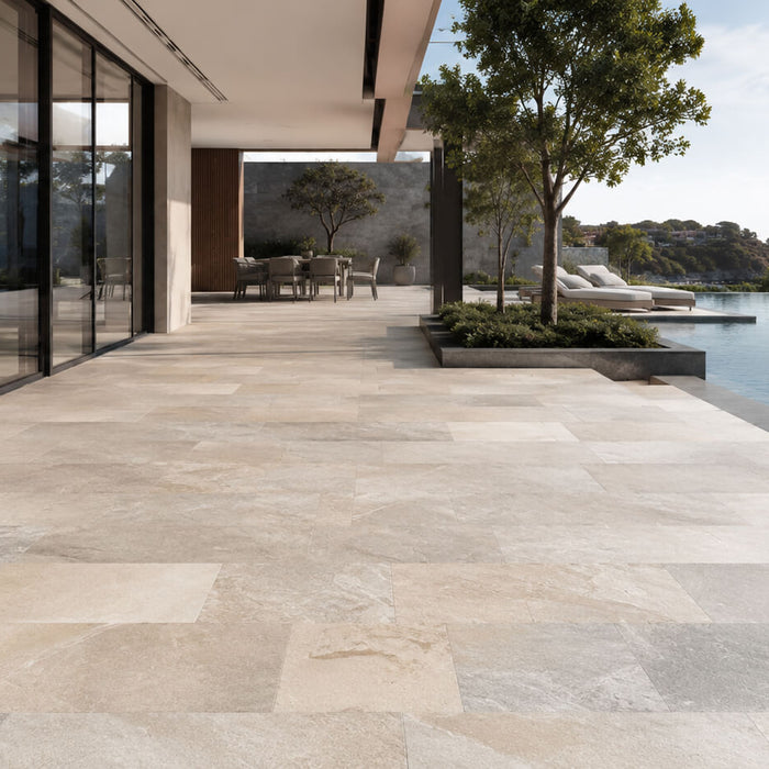 Modern villa terrace with premium natural stone pavers in warm neutral tones beside an infinity pool