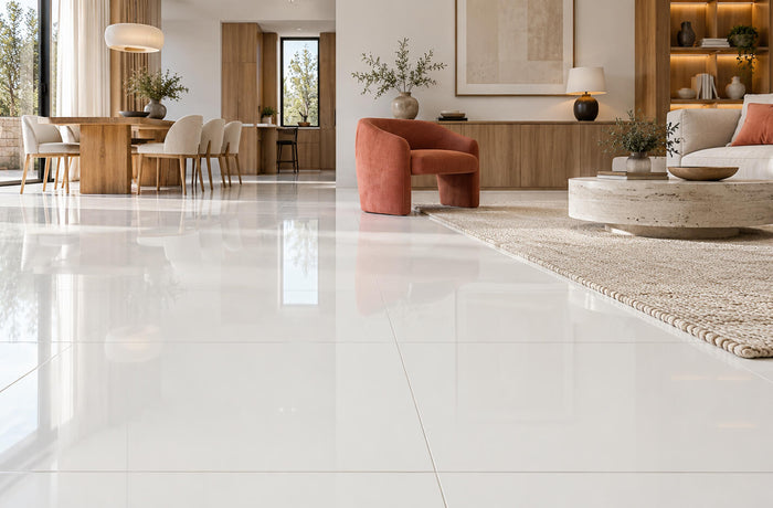 Polished white nanoglass tile flooring reflects daylight in a living room with oak cabinetry, neutral furniture, and coral accents.