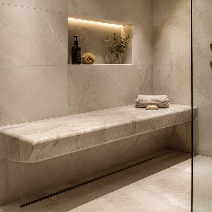 Luxury walk-in shower with a natural stone slab bench, frameless glass, warm lighting, and brass fixtures