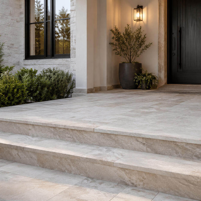 Elegant front porch with light natural stone tile, stone steps, modern dark front door, and landscaped exterior