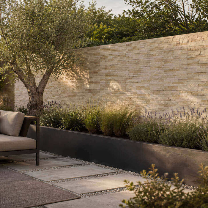 Modern garden patio with a light natural stone veneer wall, olive tree, layered planting, and neutral outdoor seating.