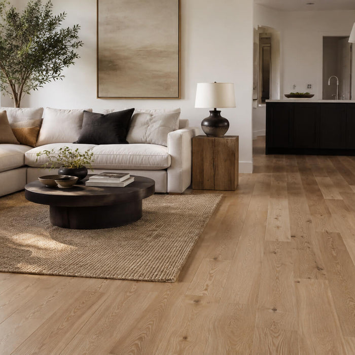 Light oak hardwood flooring in a bright open-plan living room with a modern sofa, neutral decor, and a connected kitchen area.