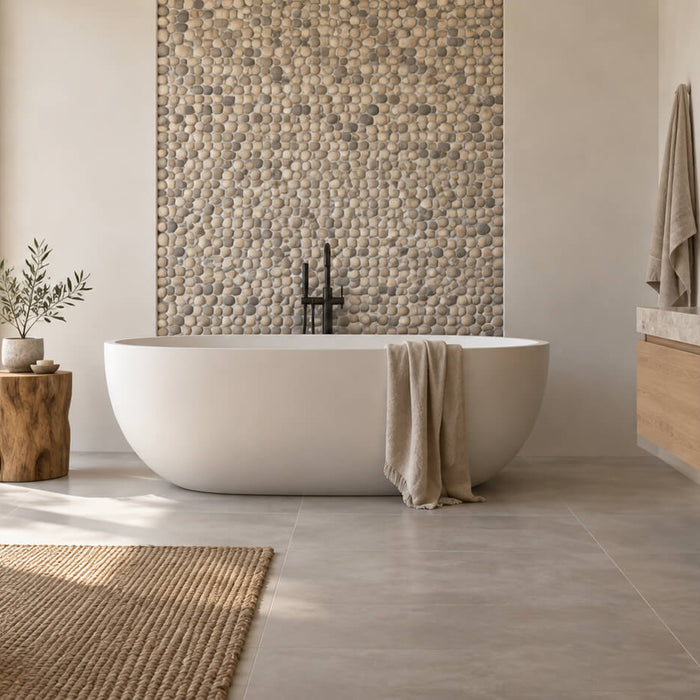 Spa-inspired bathroom with a pebble tile accent wall behind a freestanding bathtub, an oak vanity, and soft natural light.