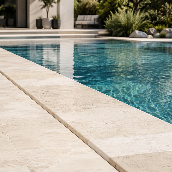 Light travertine pool coping installed around a modern backyard swimming pool