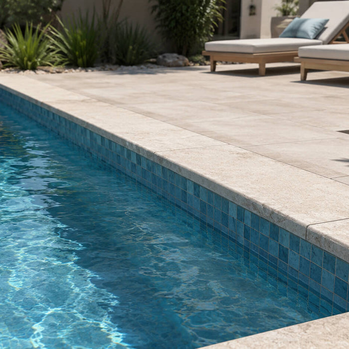 Modern swimming pool with blue waterline tile, light stone coping, and coordinated pool deck materials