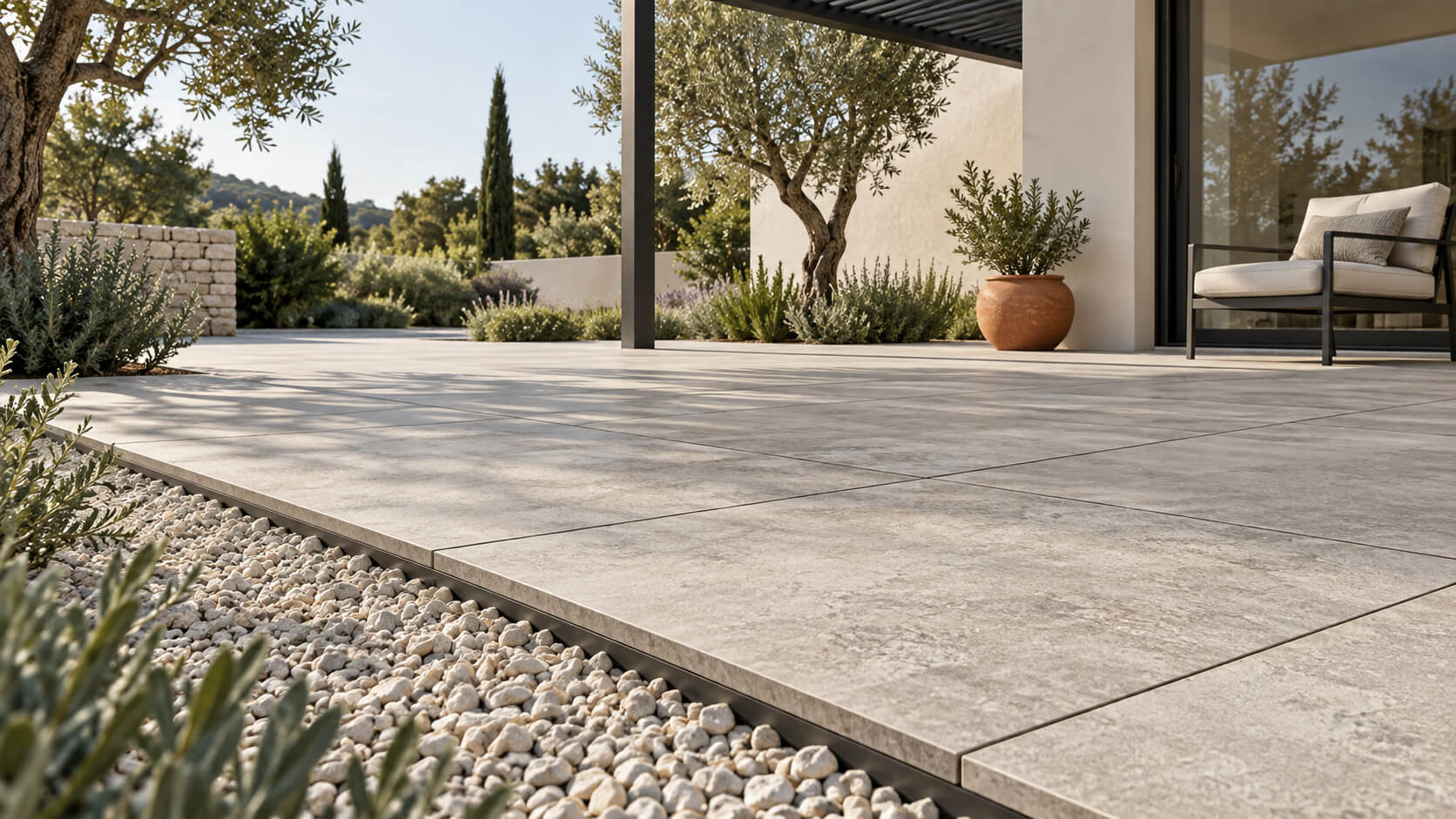 Modern courtyard with stone-look porcelain pavers, a gravel border, olive trees, and minimalist outdoor furniture.