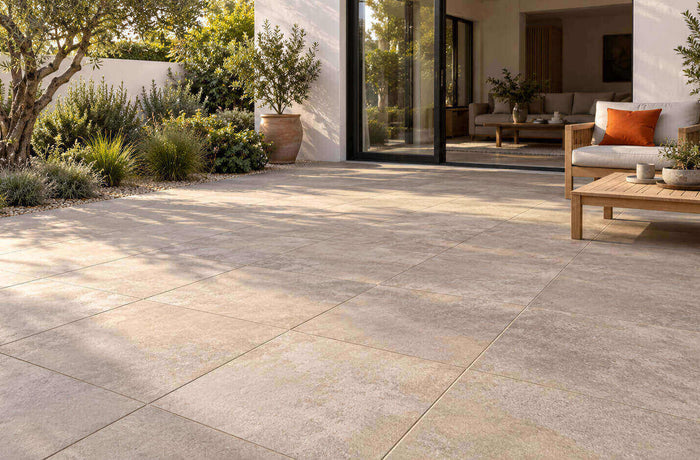 Modern patio with warm stone-look porcelain pavers, timber seating, and landscaped garden borders.