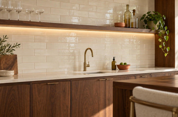 Ivory subway tile backsplash in a home bar with walnut cabinetry, a brass faucet, and warm shelf lighting.