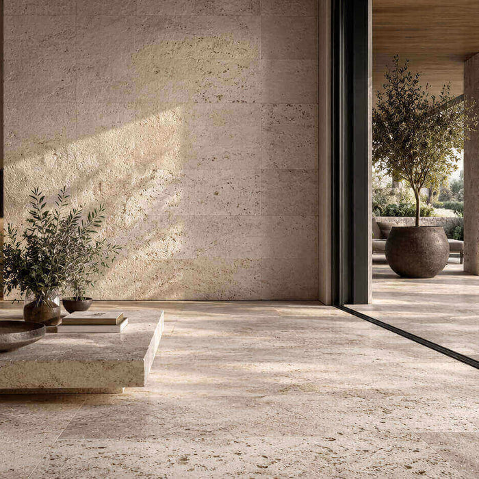 Open indoor-outdoor living space with textured natural stone floors and walls, soft natural light, and a calm luxurious design aesthetic.