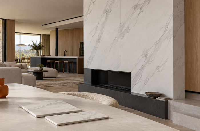 Modern living room with marble-look porcelain wall panels, oak cabinetry, and thin tile samples on a table.