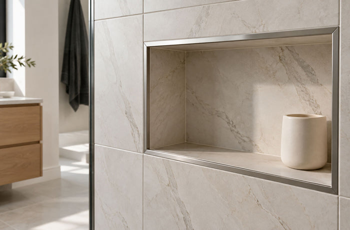 Shower niche framed with brushed metal tile edge trim, surrounded by cream stone-look tiles.