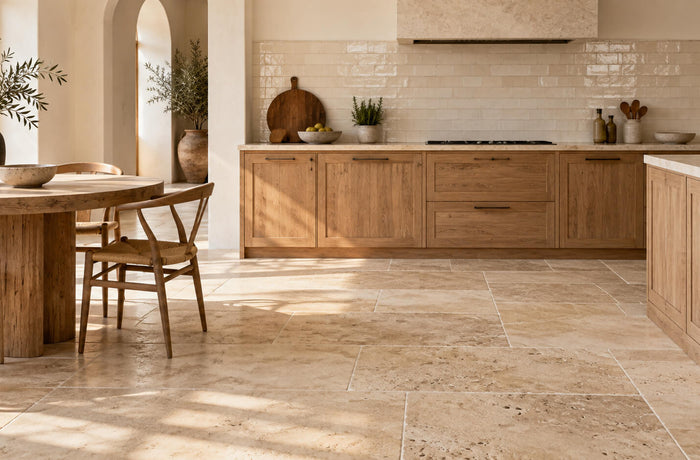 Sunlit kitchen with beige travertine floor tiles, ivory ceramic backsplash, and warm wood cabinetry.