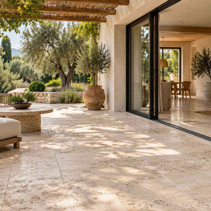 Beige travertine terrace connecting a garden home's living room with a shaded outdoor seating area.