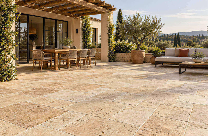 Beige travertine terrace with a wooden pergola, dining area, outdoor sofa and olive trees.