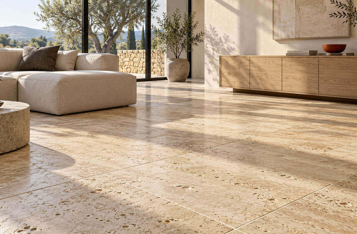 Beige travertine floor tiles in a sunlit living room with a cream sofa, oak cabinetry, and large windows.