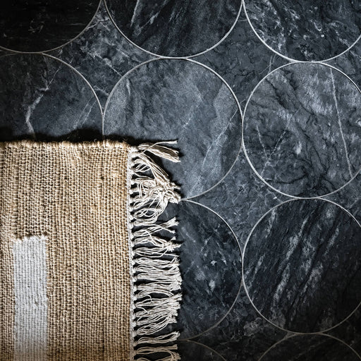 Blendables Talking in Circles Flannel 10x10 honed marble tile with dark gray veining and a circular pattern beside a beige rug.