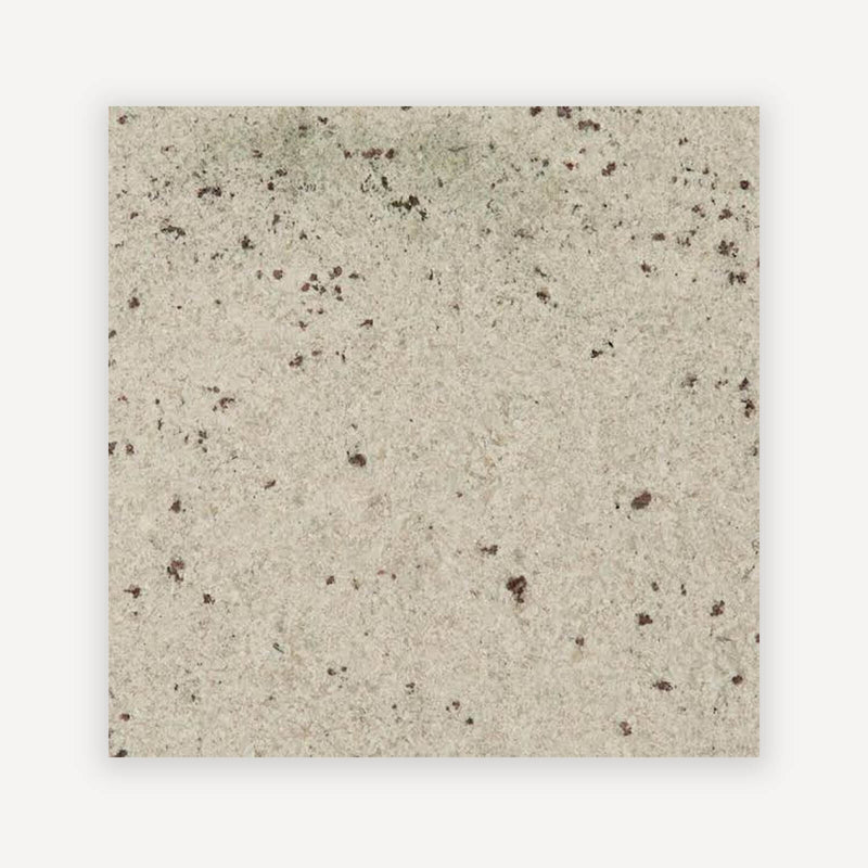 Colonial White granite with a cream-white base and scattered dark burgundy mineral flecks.