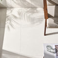 Corinthian White 24x24 filled and honed limestone flooring beside a wooden chair, with natural sunlight and soft leaf shadows.