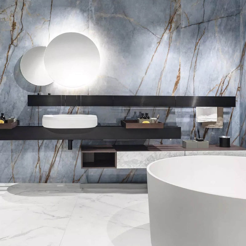 Florim Heritage Azure porcelain bathroom walls behind a floating vanity, round mirrors and a white freestanding bathtub.