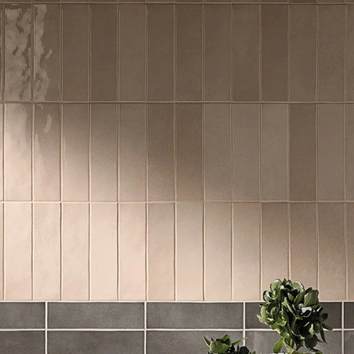 Highland Lake Almond glossy ceramic wall tiles installed vertically above gray tiles beside a green plant.