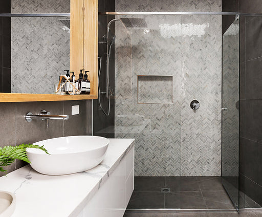 Modern bathroom with gray herringbone marble shower tile, glass enclosure, and white vanity.