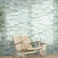 Mayolica Beret Tea 2x6 glossy ceramic tiles on a green wall behind a woven chair and side table.