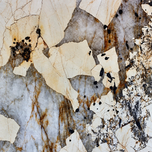 Patagonia polished granite slab with cream sections, gray crystalline areas, amber veining and dark mineral inclusions.