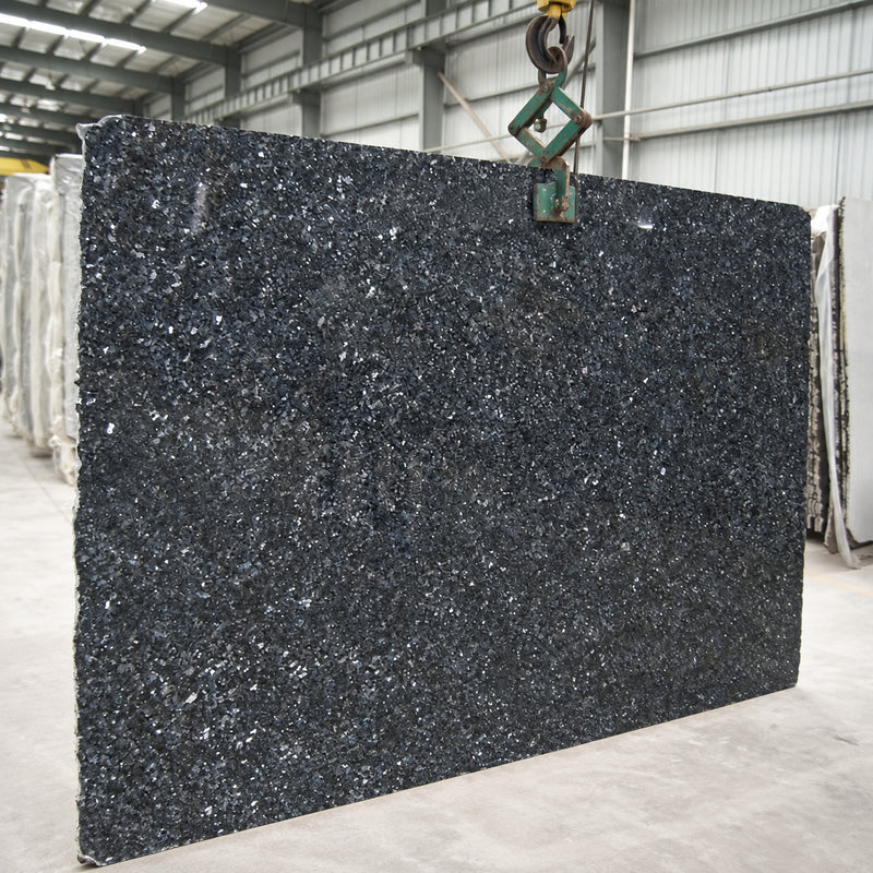 Silver Pearl granite slab with a dark charcoal surface and bright silver mineral flecks in a stone warehouse.