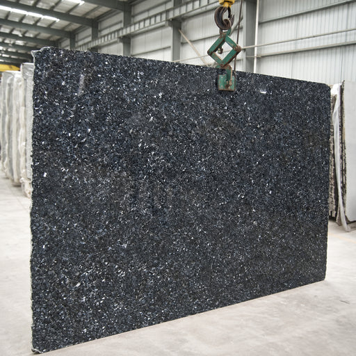 Silver Pearl granite slab with a dark charcoal surface and bright silver mineral flecks in a stone warehouse.