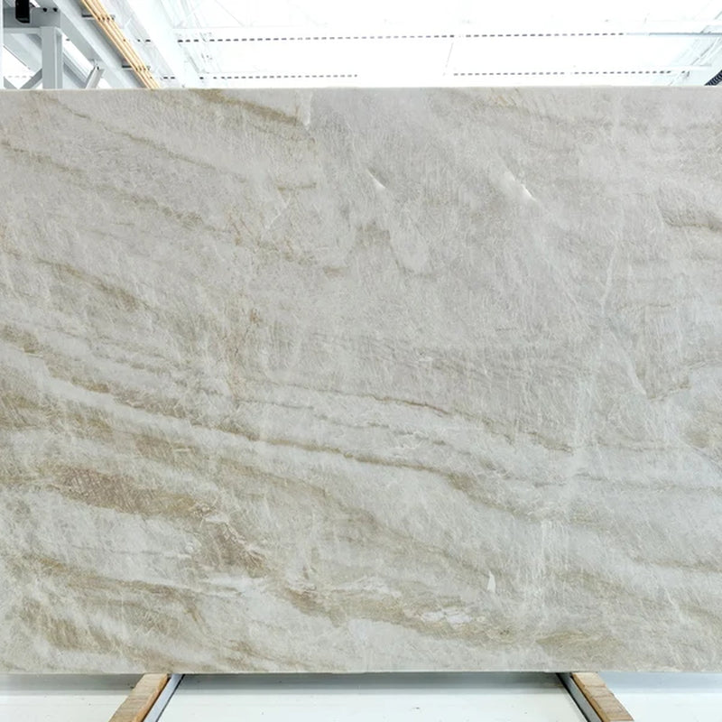 Montebello honed quartzite slab with sweeping beige and gray veins in a warehouse.
