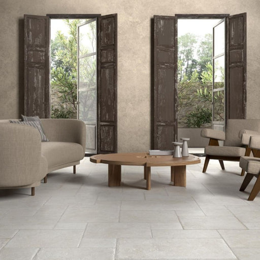 Unicom Pierre Neuve Blanc Multiformato matte porcelain floor tiles in a mixed-size layout beneath a wooden coffee table and neutral seating.