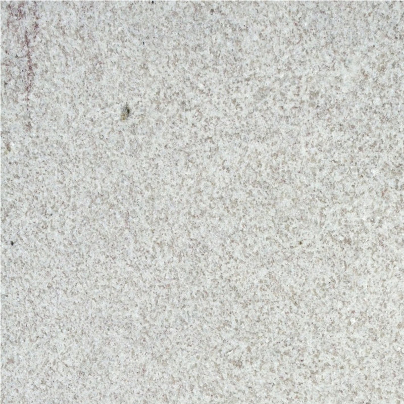 Close-up of White Fantasy granite with a pale white surface, fine gray speckling, and subtle lavender veining.