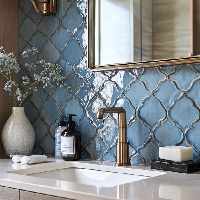 A bathing room with lavish moonlight blue arabesque mosaic tiles in front of  a gold tipped mirror.